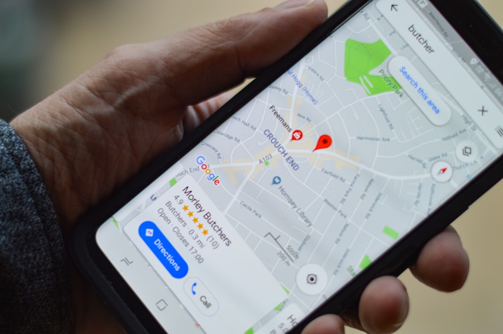 A hand holding a smartphone showing a map with search results, similar to searching for a traveller's route